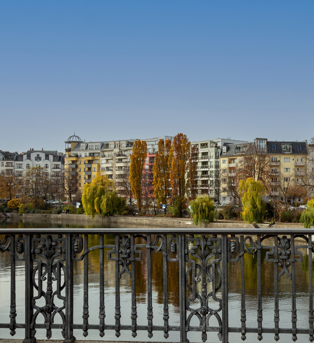 Ausschnitt vom Berliner Stadtbild an einem See, im Vordergrund ein nur wenig herausragendes Eisengeländer.